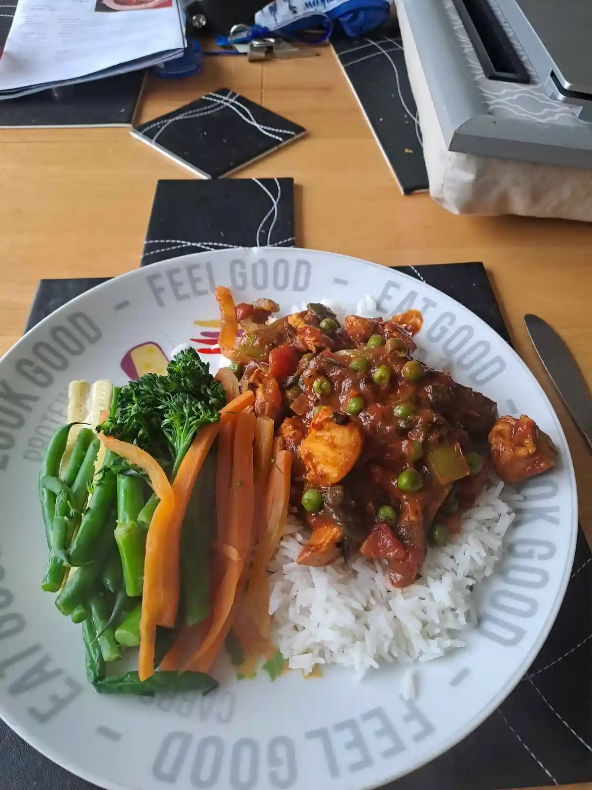 A plate of food with white rice, a meaty curry with peas and vegetables, and a side of green beans, carrots, and broccoli…