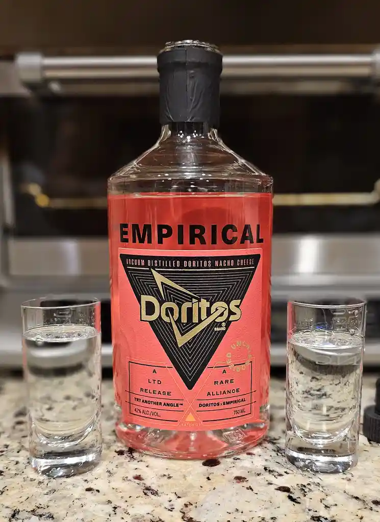 A clear glass bottle labeled 'EMPIRICAL' with a red label featuring the Doritos logo and text 'VACUUM DISTILLED DORITOS…
