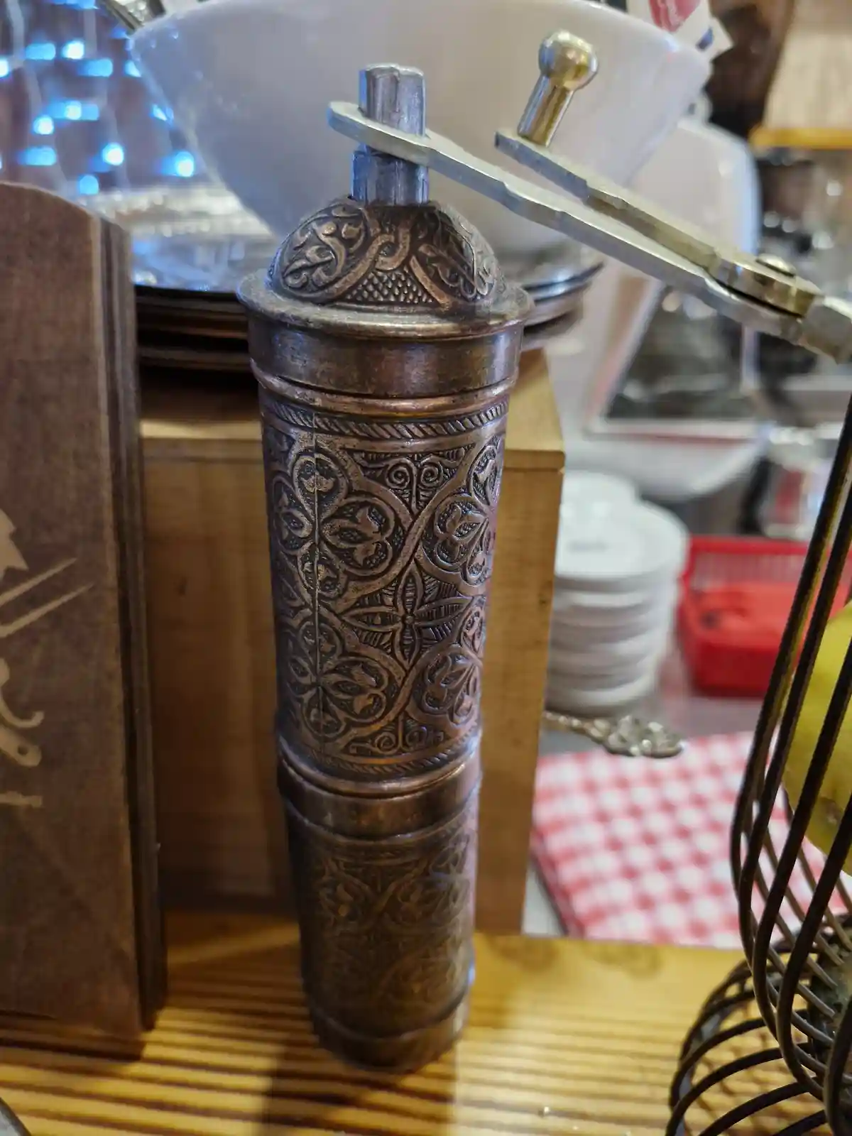 A close-up photo shows an ornate, antique-style metal pepper mill with intricate scrollwork, sitting on a wooden counter in…