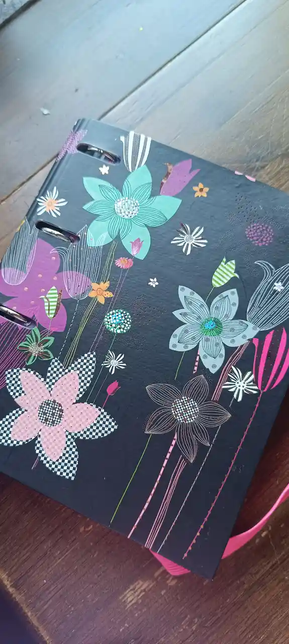 A dark gray binder with a colorful floral pattern featuring large and small flowers in pink, teal, white, and purple, some…