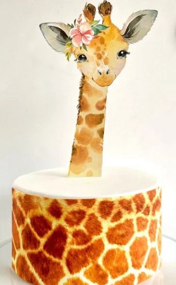 A cake decorated to look like a giraffe, with a giraffe head topper adorned with a pink flower crown, standing atop a…