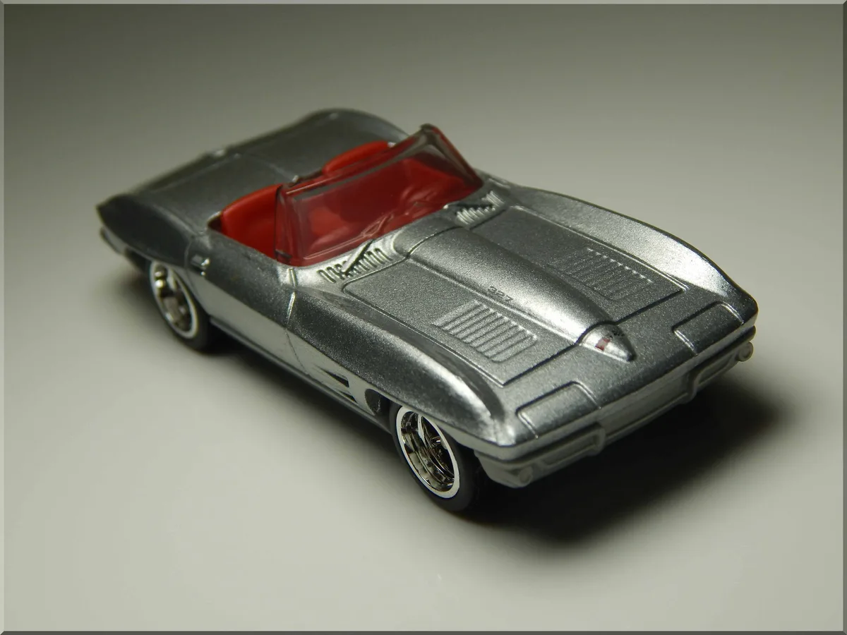A silver die-cast toy car, resembling a classic convertible, is photographed on a plain gray background. The car has red…