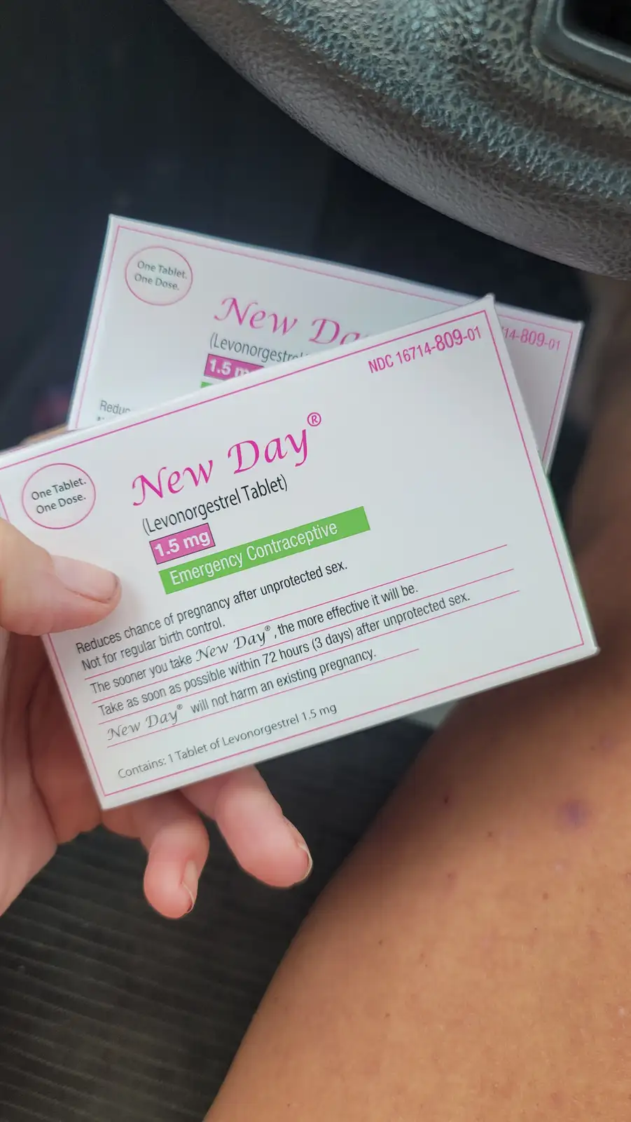 A hand holds two boxes of 'New Day' emergency contraceptive pills inside a car, with the packaging clearly visible showing…