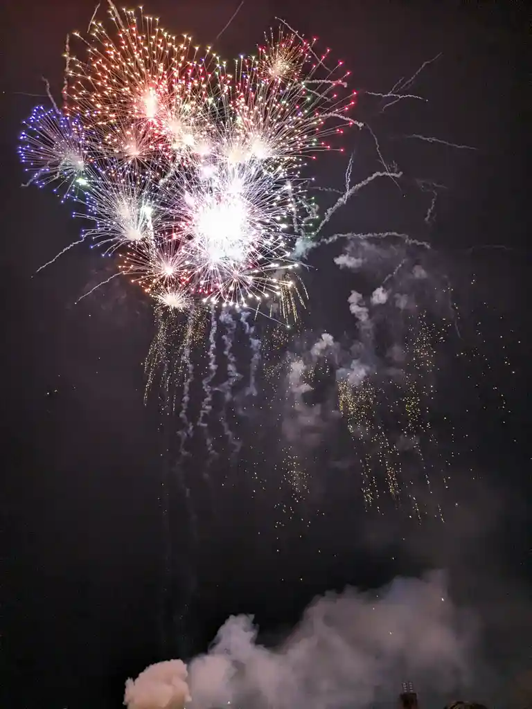 A vibrant nighttime photograph captures a massive, colorful fireworks explosion in the sky, with bursts of red, white, blue…
