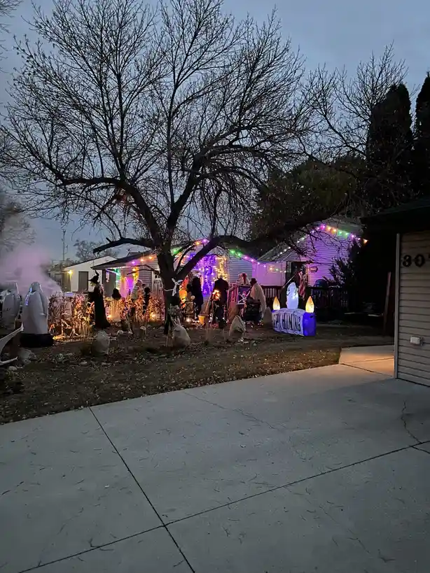 A residential front yard at dusk is heavily decorated for Halloween with numerous inflatable figures, including ghosts and a…