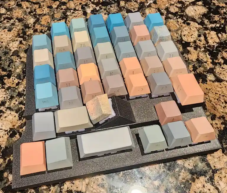 A custom mechanical keyboard with pastel-colored keycaps arranged in a gradient of blues, beiges, and peaches sits on a…