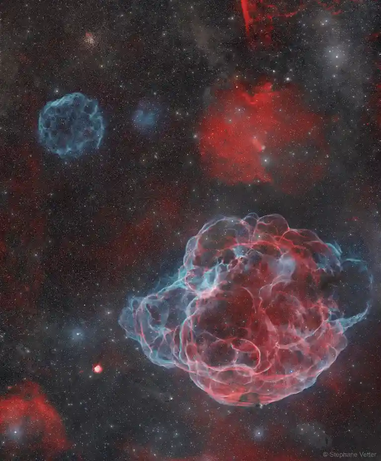 A space photograph shows colorful nebulae in red and blue against a starry black background. The largest nebula in the…