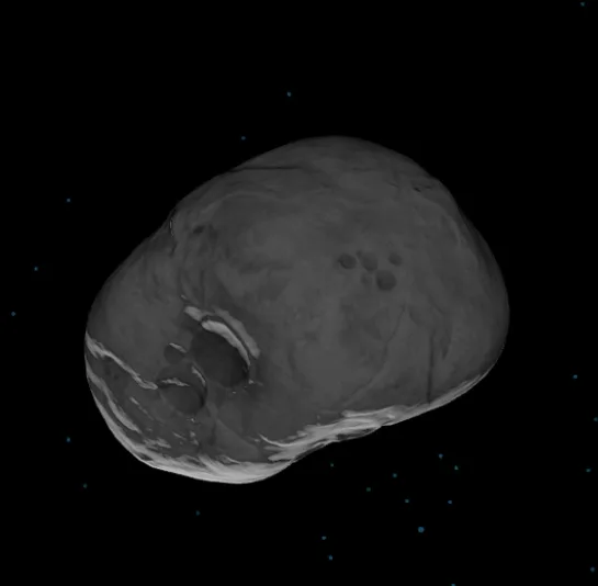 A grayscale image of a large, irregularly shaped asteroid floating in space against a black background with scattered blue…