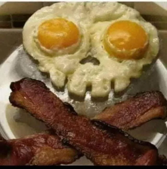 a plate of breakfast food arranged to resemble a skull: two fried eggs with yolks forming the eyes and the egg whites…