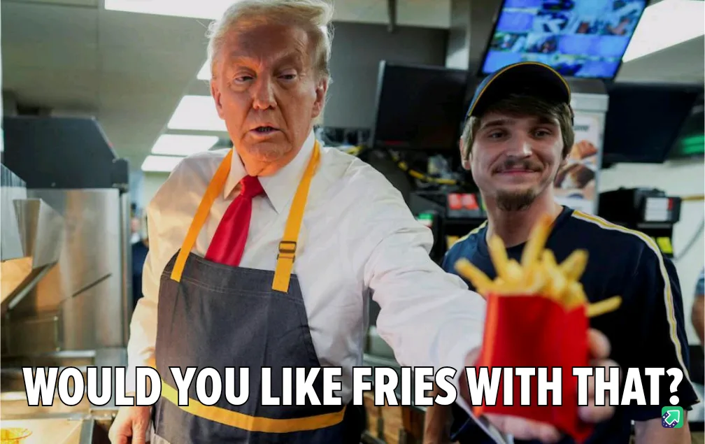 A man in a fast-food worker's apron and red tie holds out a container of fries while looking at the camera. Behind him…