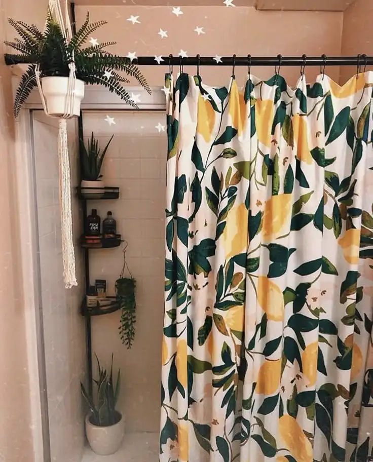 A bathroom with a shower curtain featuring a yellow lemon and green leaf pattern, surrounded by multiple potted plants on…