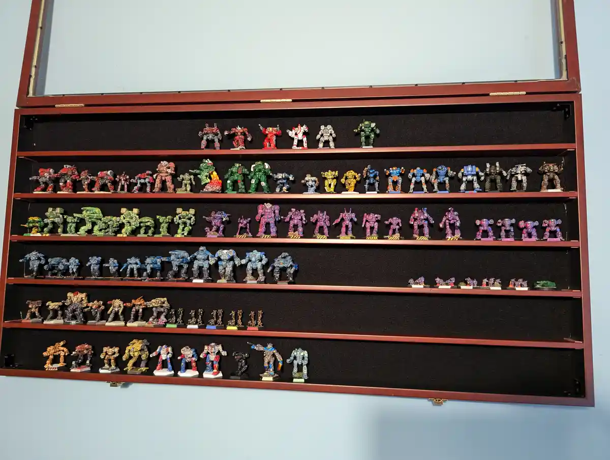 A large, open wooden display case mounted on a light blue wall contains six shelves filled with dozens of painted, humanoid…