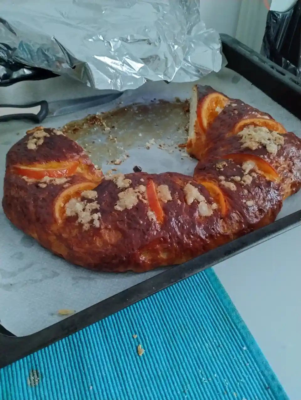A golden-brown, circular baked good, resembling a wreath or braided bread, sits on a baking tray lined with parchment paper…