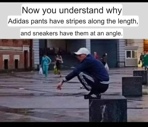 A man in a blue Adidas tracksuit with white stripes and a white cap is crouching on a low stone block in a public plaza. He…
