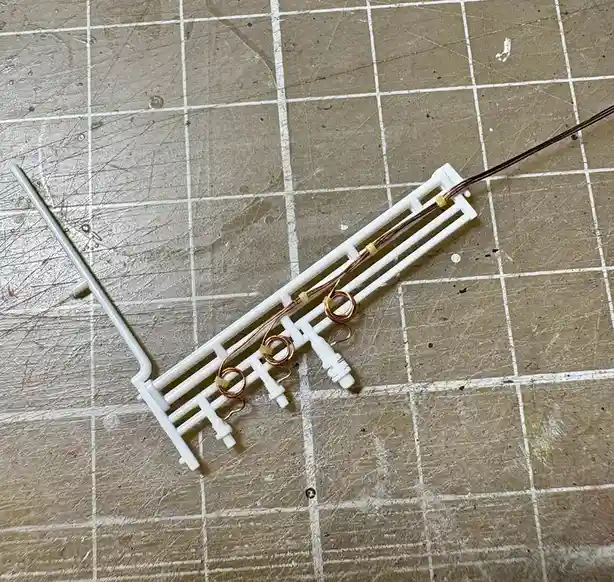 A white plastic keyboard keycap frame with copper wires coiled and taped to its structure lies on a scratched, grid-lined…