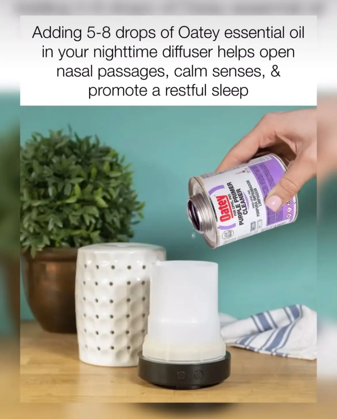 A hand pours liquid from a can labeled 'Oatey Purple Primer Cleaner' into a white electric diffuser on a wooden table. In…
