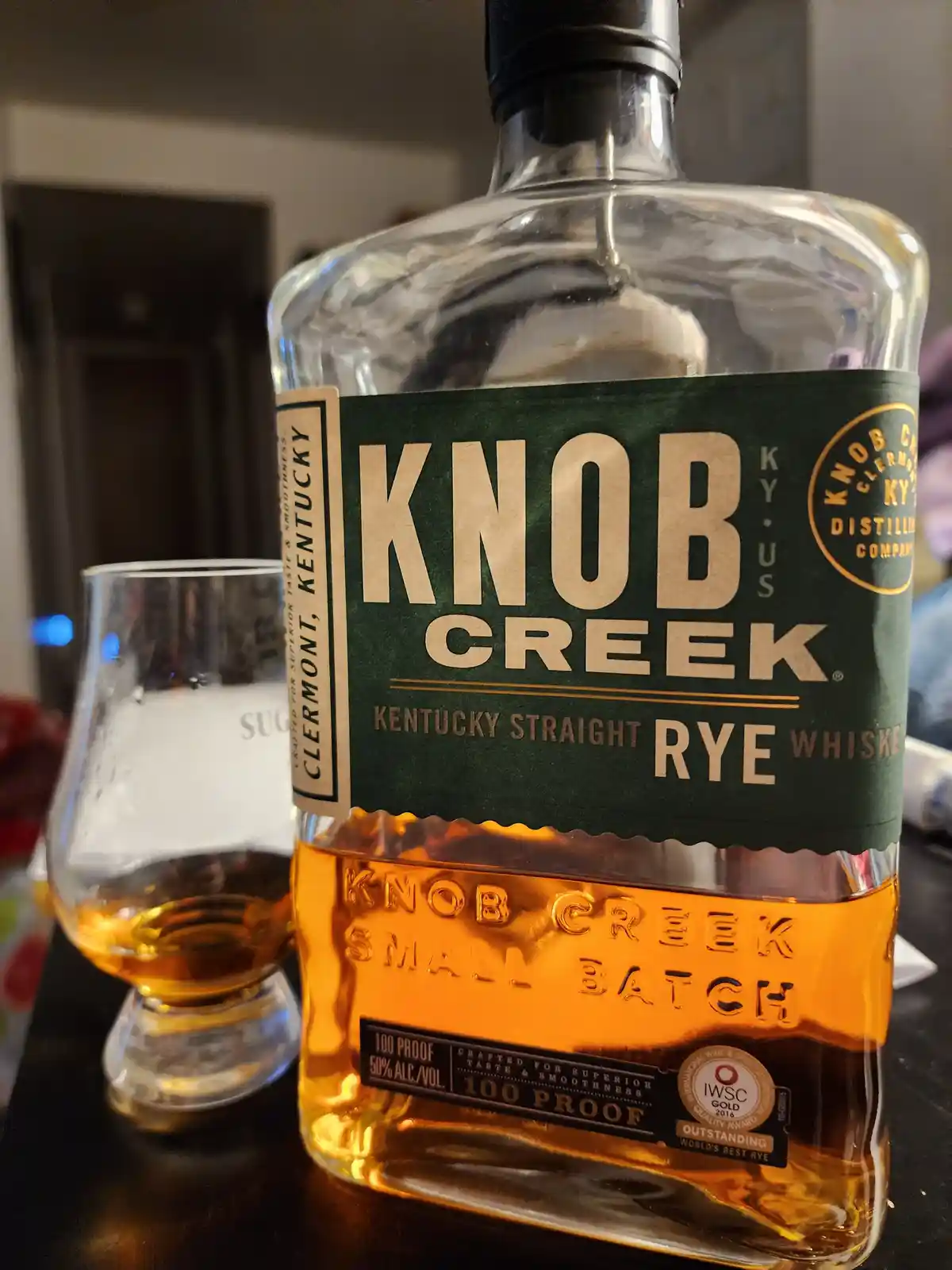 A close-up photo shows a bottle of Knob Creek Kentucky Straight Rye Whiskey, 100 proof, next to a tasting glass containing a…