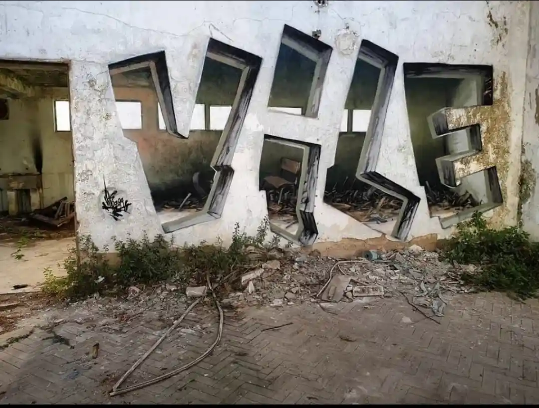 An abandoned, dilapidated building interior with large, three-dimensional letters spelling 'VILE' carved into the wall…