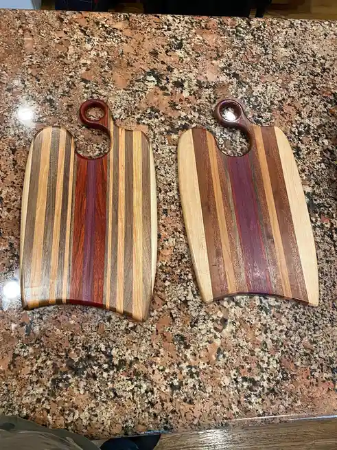Two wooden cutting boards with striped patterns sit side-by-side on a speckled granite countertop. The boards are nearly…