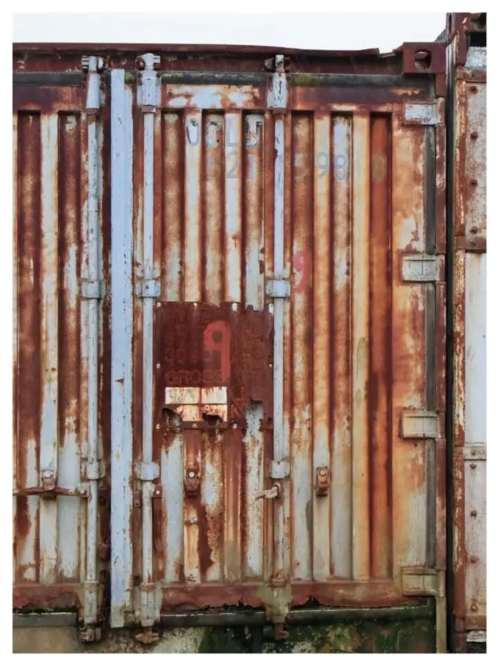 A close-up of a heavily rusted, weathered shipping container door with faded markings and a large, faded red number '9'…