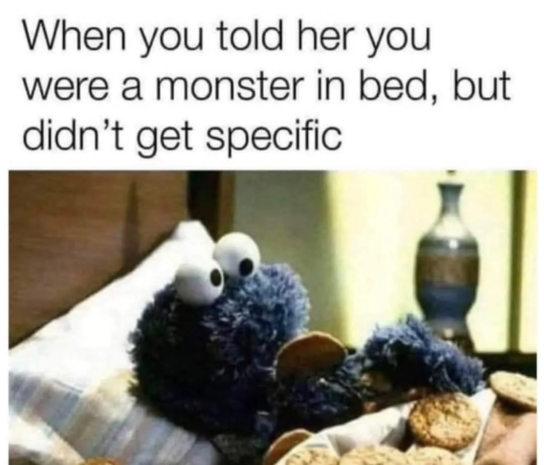 A blue, furry monster puppet with large white eyes sits in bed surrounded by cookies, looking guilty or embarrassed. The…