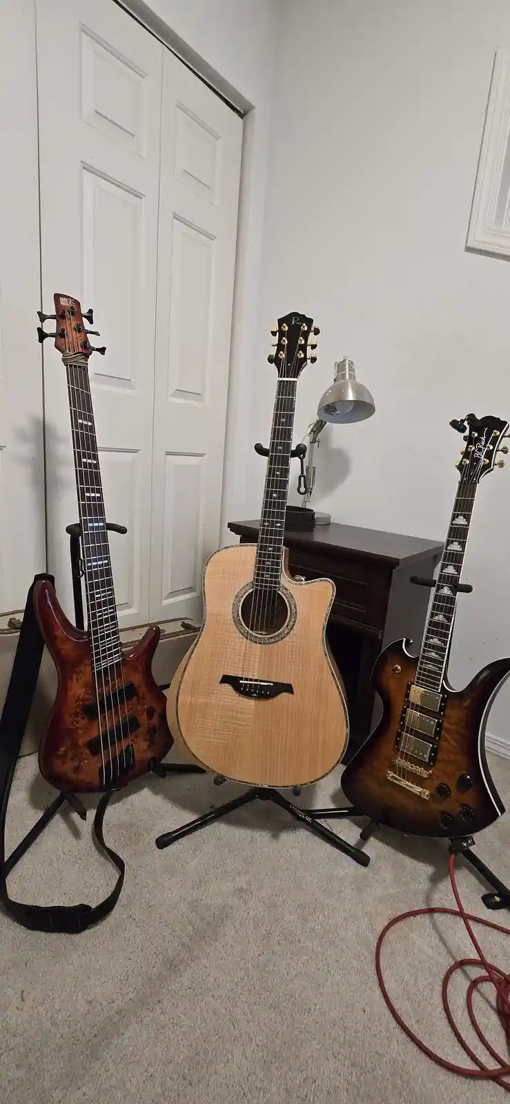 Three stringed instruments—a bass guitar, an acoustic guitar, and an electric guitar—are standing upright on stands in a…