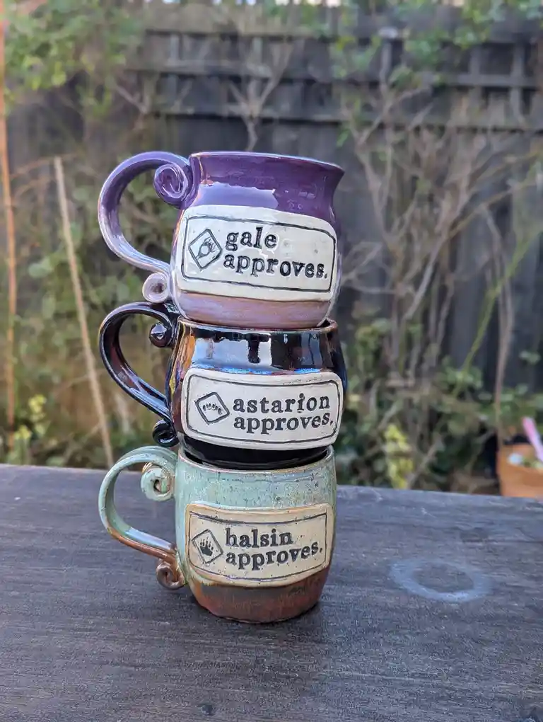 Three hand-painted ceramic mugs are stacked on a wooden surface outdoors, each with a label reading 'gale approves.'…