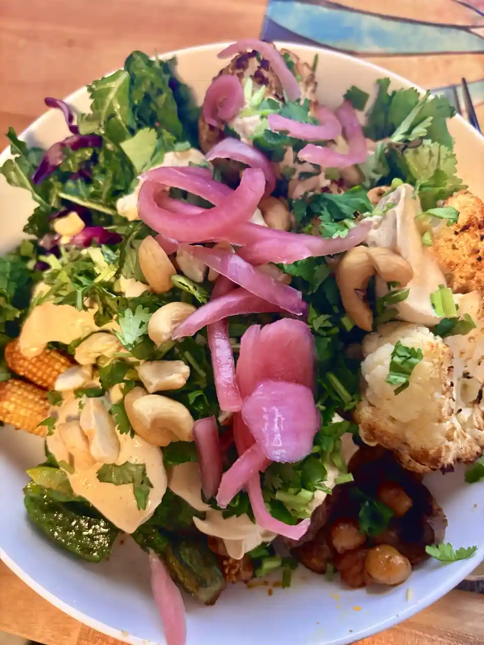 A close-up photo of a colorful, healthy-looking salad in a white bowl, featuring mixed greens, roasted cauliflower…