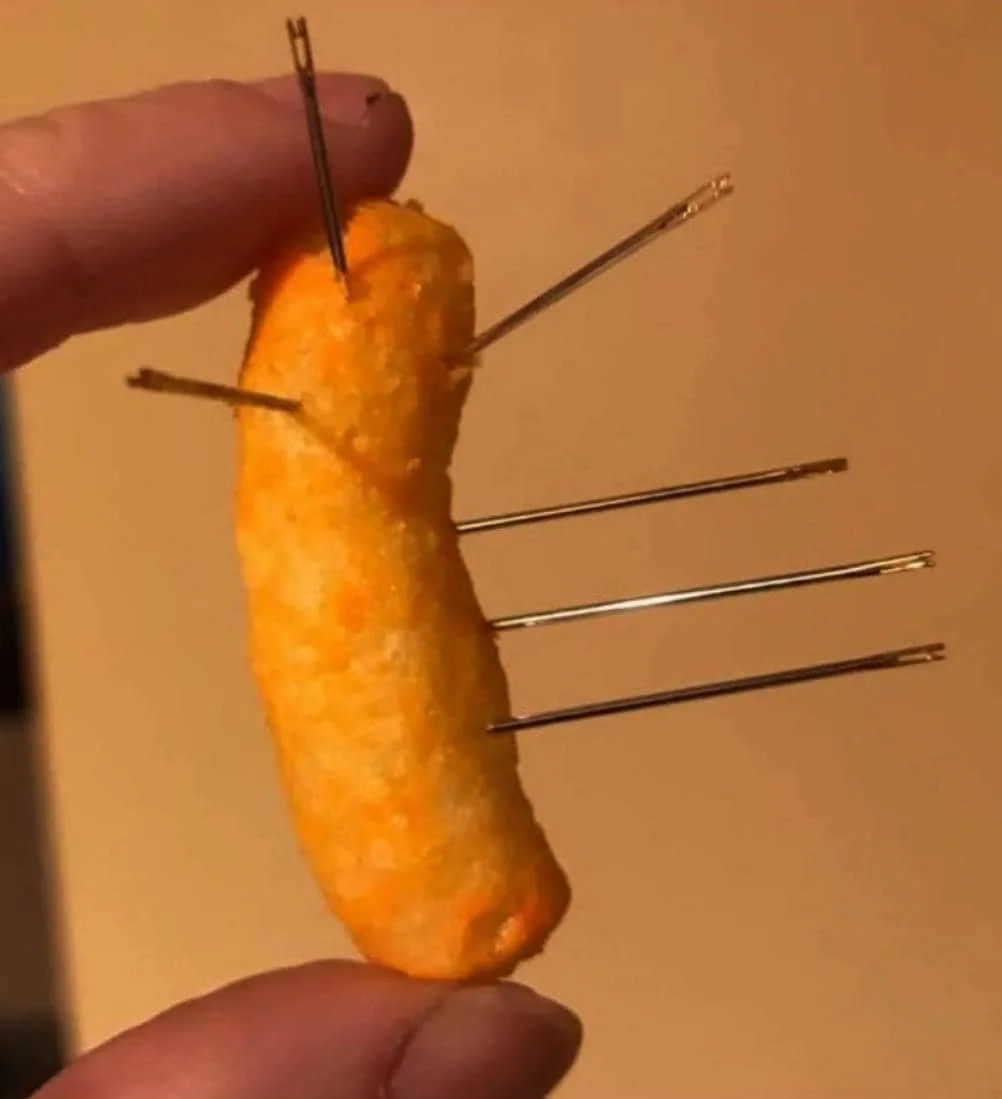 A close-up photo shows a person holding a single orange, puffy, cheese-flavored snack stick, resembling a Cheeto. Five thin…
