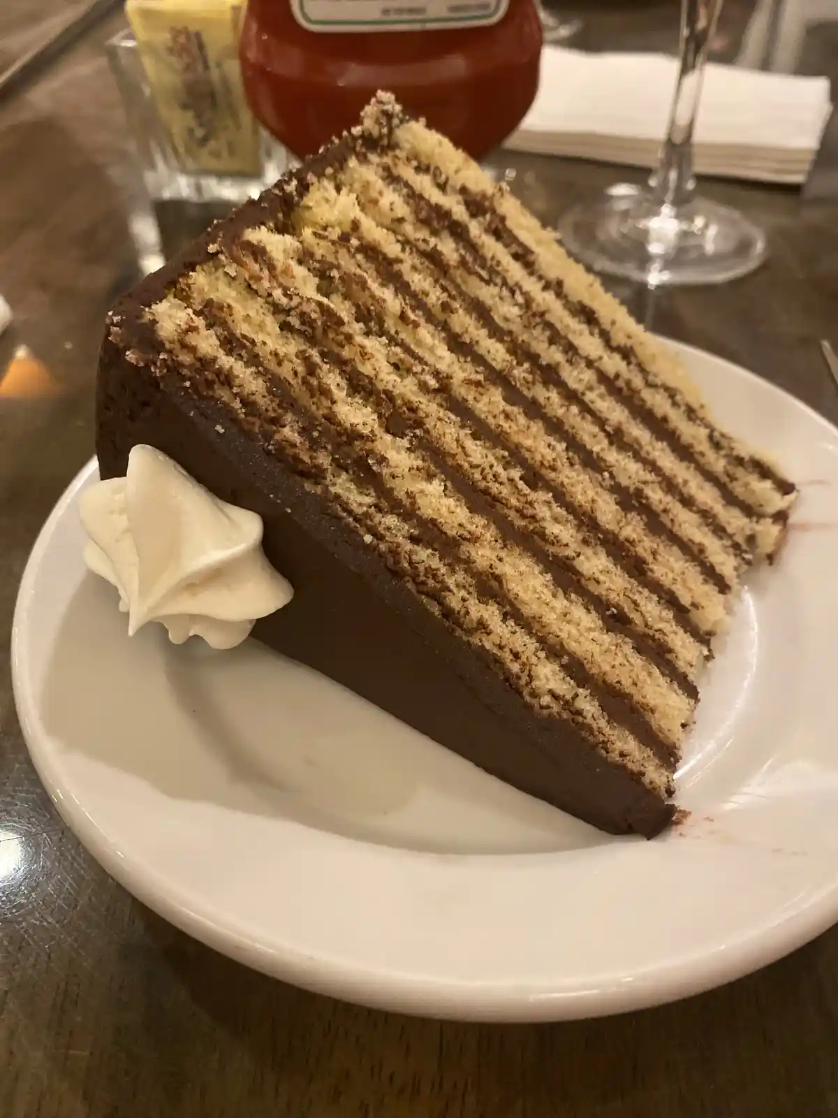 A close-up photo shows a slice of multi-layered chocolate cake with alternating light cake and dark chocolate frosting…