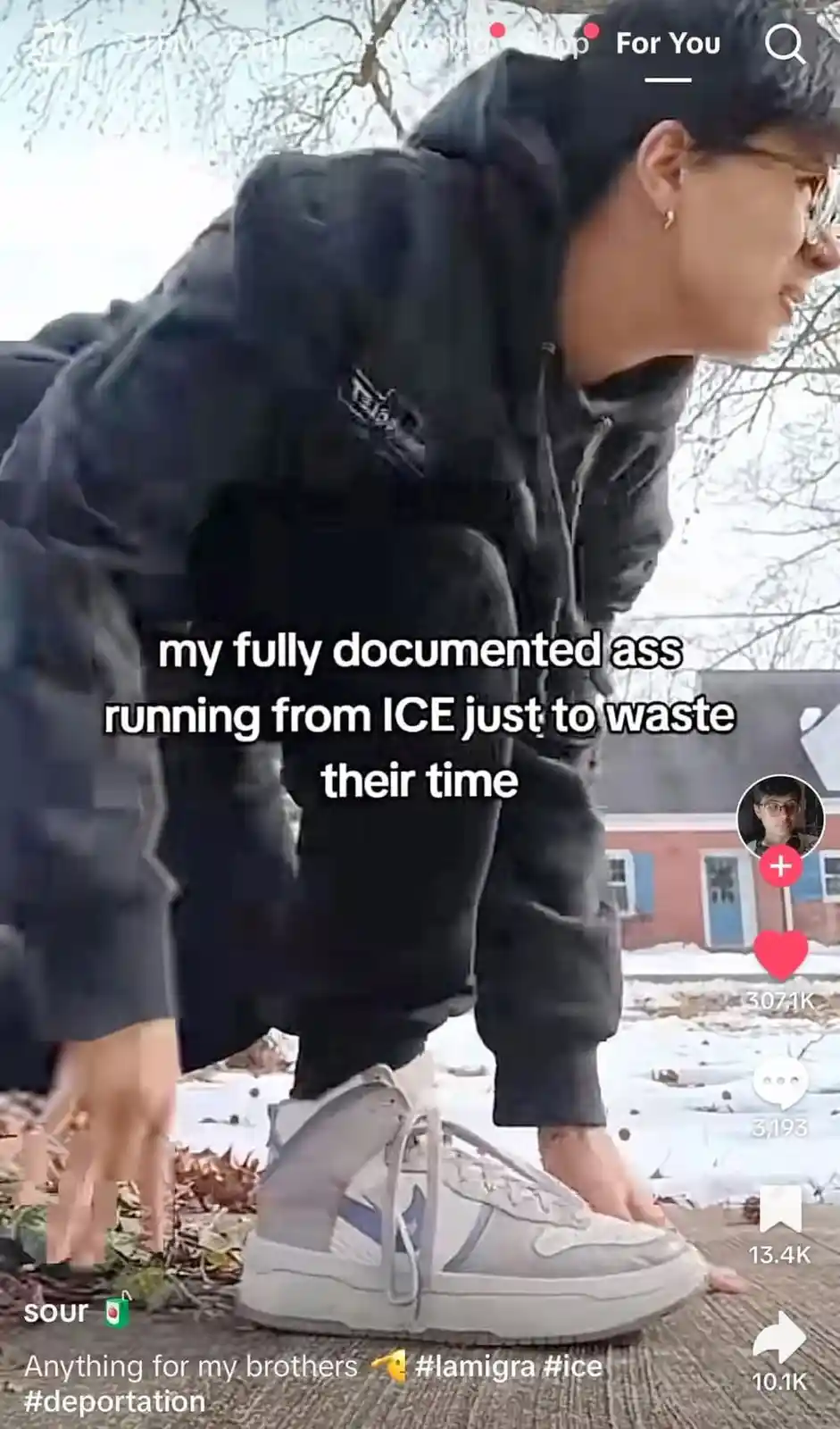 A person in a black hoodie and grey sneakers is crouching outdoors on a snowy path, hands on the ground as if preparing to…