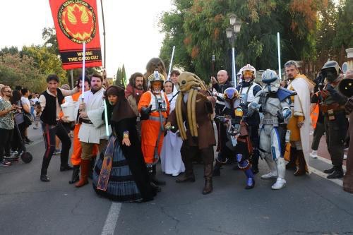 A group of people dressed as Star Wars characters, including Jedi, Stormtroopers, and other figures, stand together outdoors…