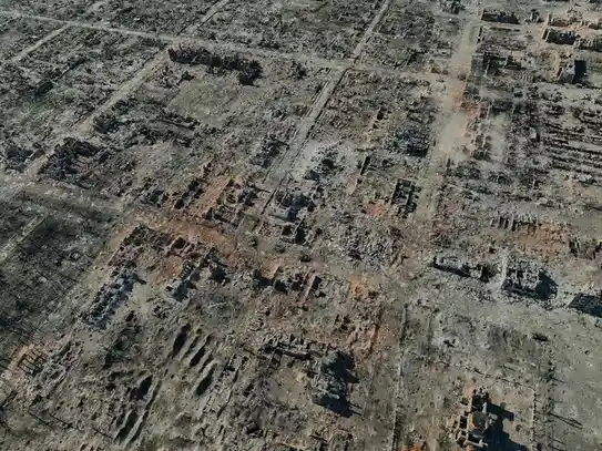 An aerial view shows a cityscape reduced to rubble and ash, with streets and building foundations barely visible beneath the…