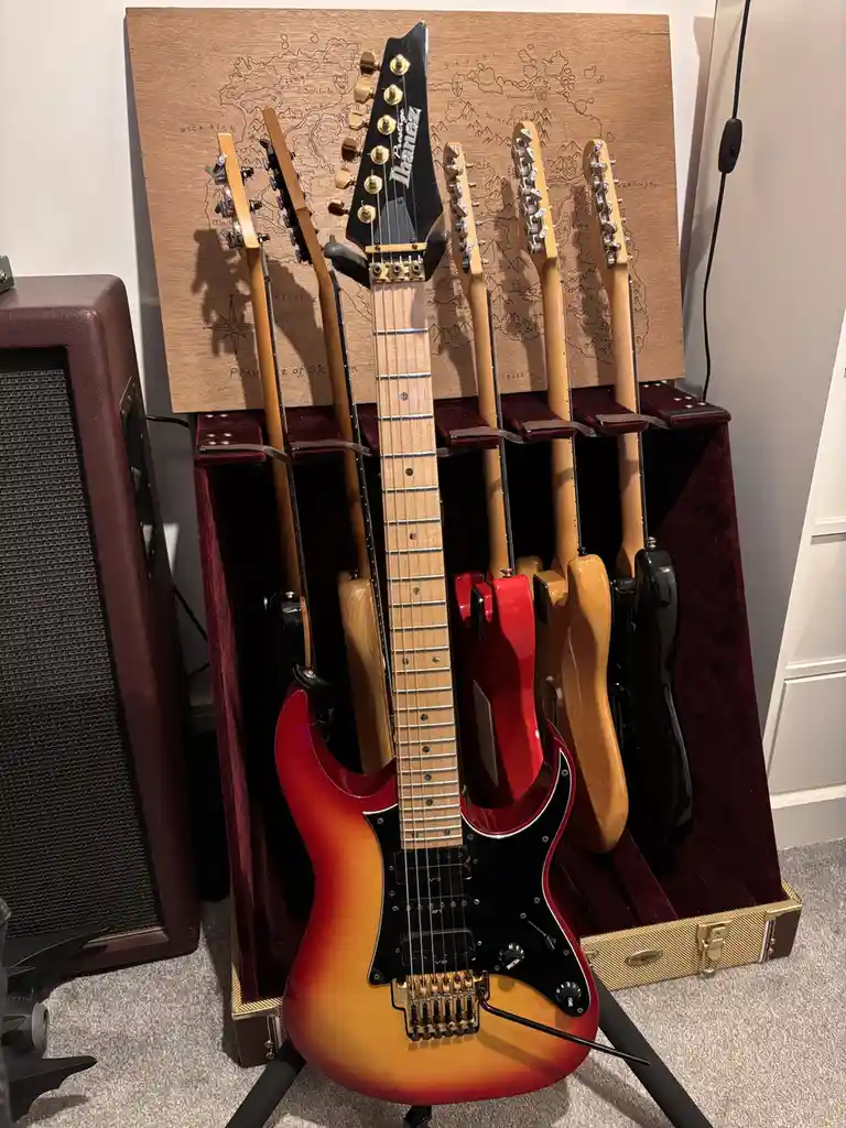 A collection of electric guitars, including a prominent red and black Ibanez, are displayed upright in a custom wooden stand…