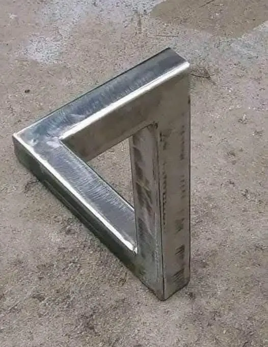 A 3D metal sculpture of an impossible triangle, also known as a Penrose triangle, rests on a concrete floor. The overlaid…