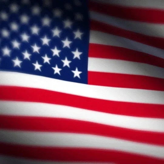 A close-up, slightly blurred image of the American flag waving, showing the blue canton with white stars and red and white…