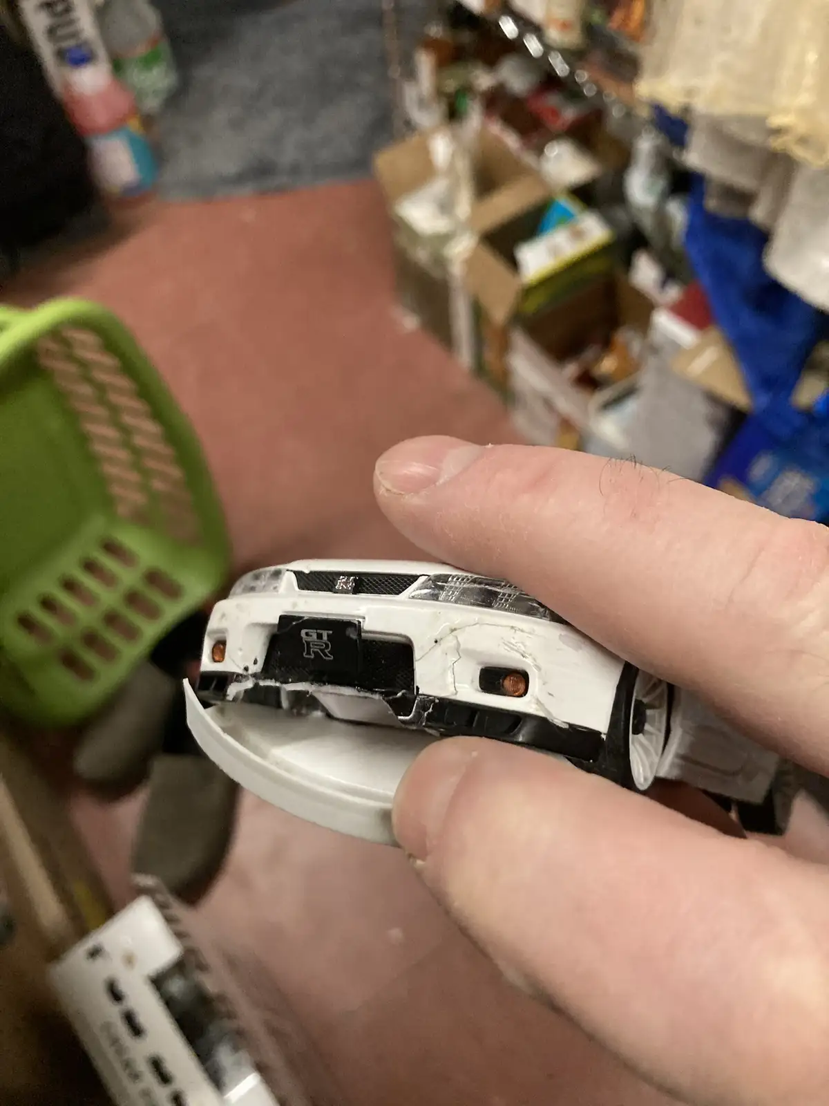 A hand holds a small, white toy car with visible damage to its front bumper and grille, revealing the 'GT R' logo…
