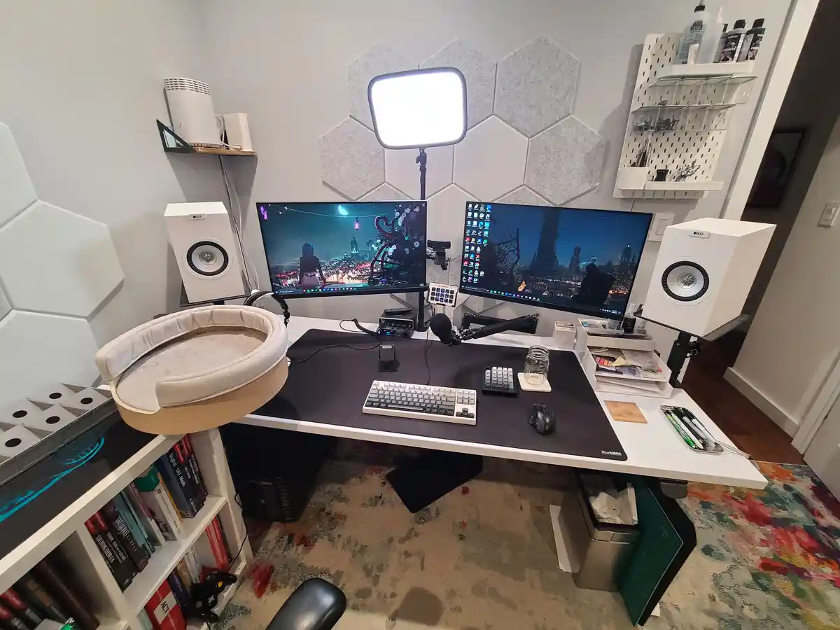 A well-organized, modern home office setup with two large monitors, white speakers, a bright LED light, and a keyboard on a…