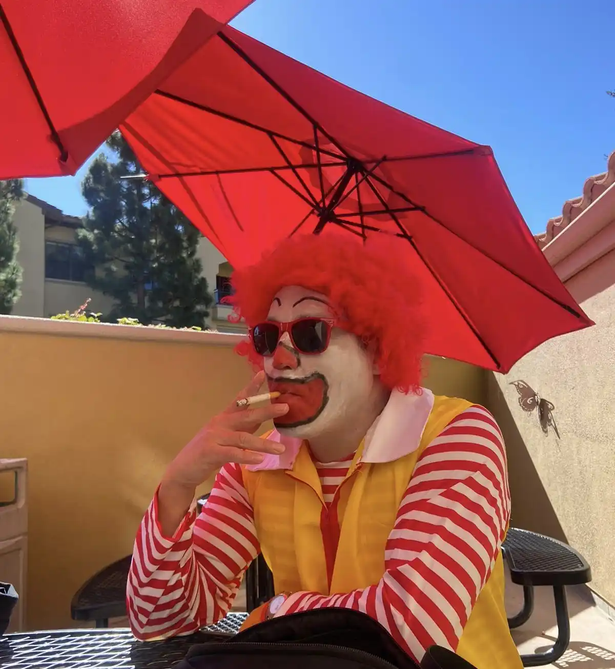 A person dressed as Ronald McDonald, complete with red wig, white face paint, red nose, and red-and-white striped shirt…