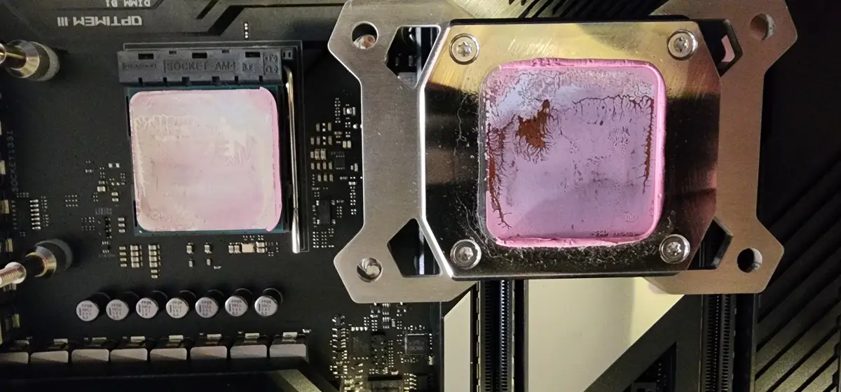 A close-up photo of a computer motherboard showing two square pink thermal paste blobs on CPU and GPU mounting points. The…