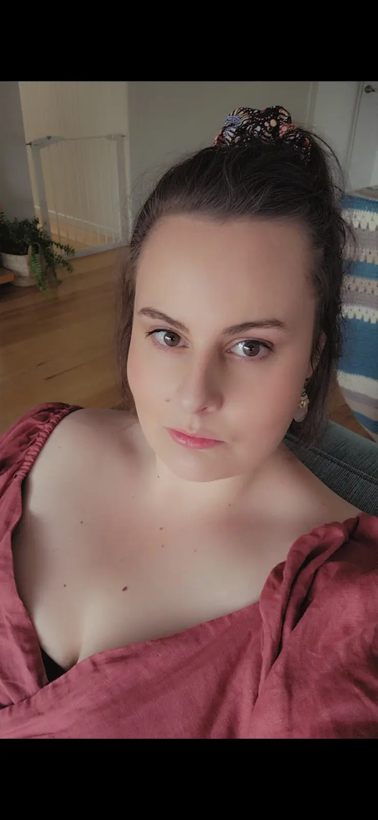 A woman with dark hair tied up with a patterned scrunchie stares directly at the camera with a neutral, slightly unimpressed…