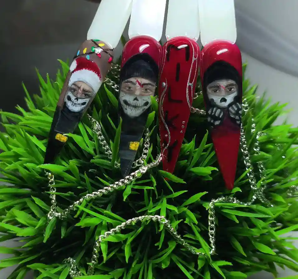 Five long, pointed artificial nails are displayed on a bed of green artificial grass, each decorated with a different…