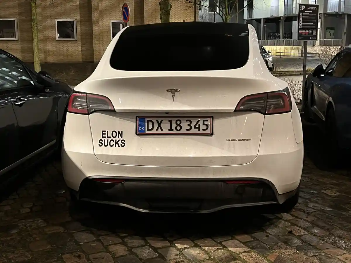 The rear view of a white Tesla Model X parked on a cobblestone street at night, featuring a Danish license plate (DK DX 18…