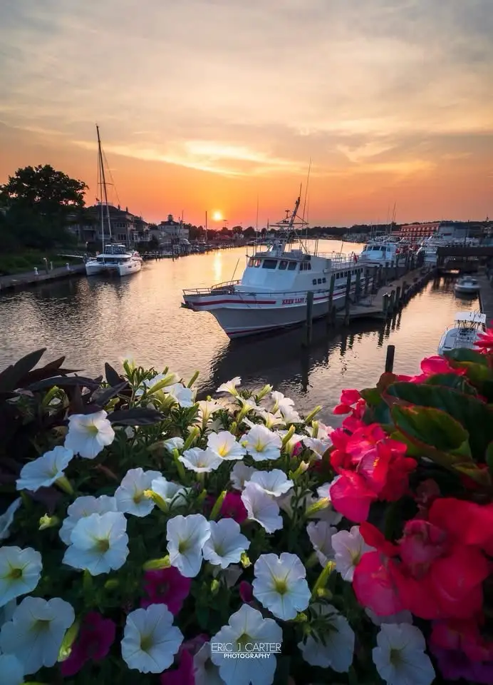 A scenic sunset photograph of a harbor with boats docked, including a prominent white vessel labeled 'KEEP LADY'. In the…