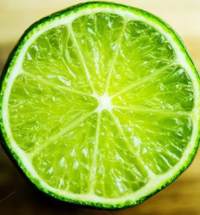 A close-up photo shows a cross-section of a bright green lime, revealing its segmented, juicy interior and dark green rind…
