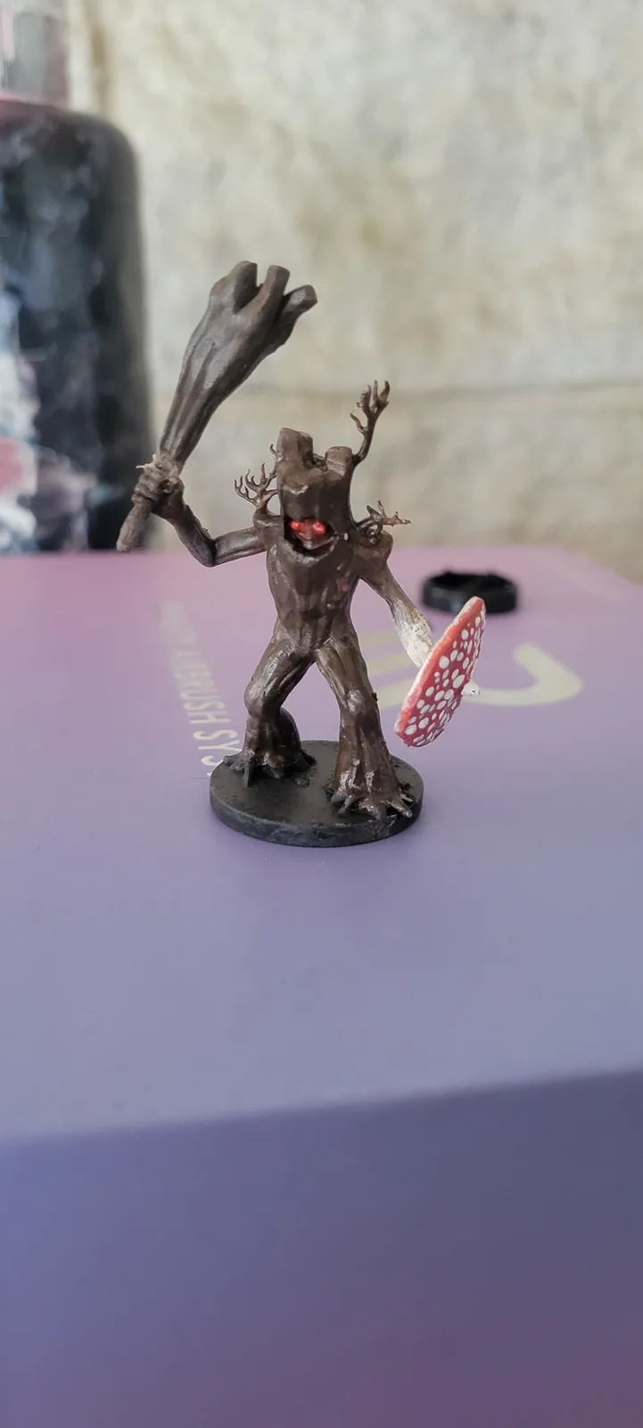 A brown, tree-like fantasy miniature figure with glowing red eyes, antler-like protrusions, and a menacing expression stands…