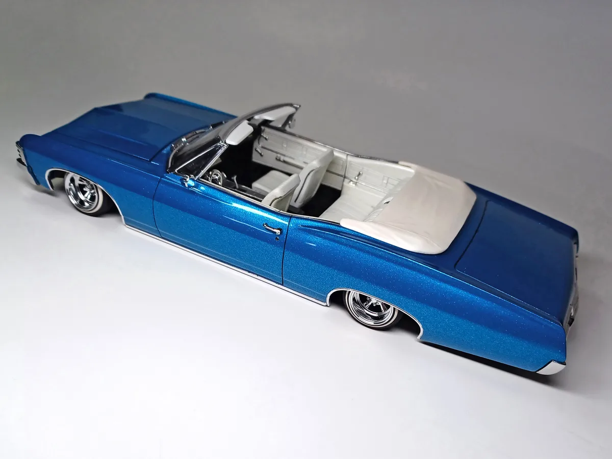 A blue metallic die-cast model of a classic American convertible car with its top down, revealing a white interior, posed on…