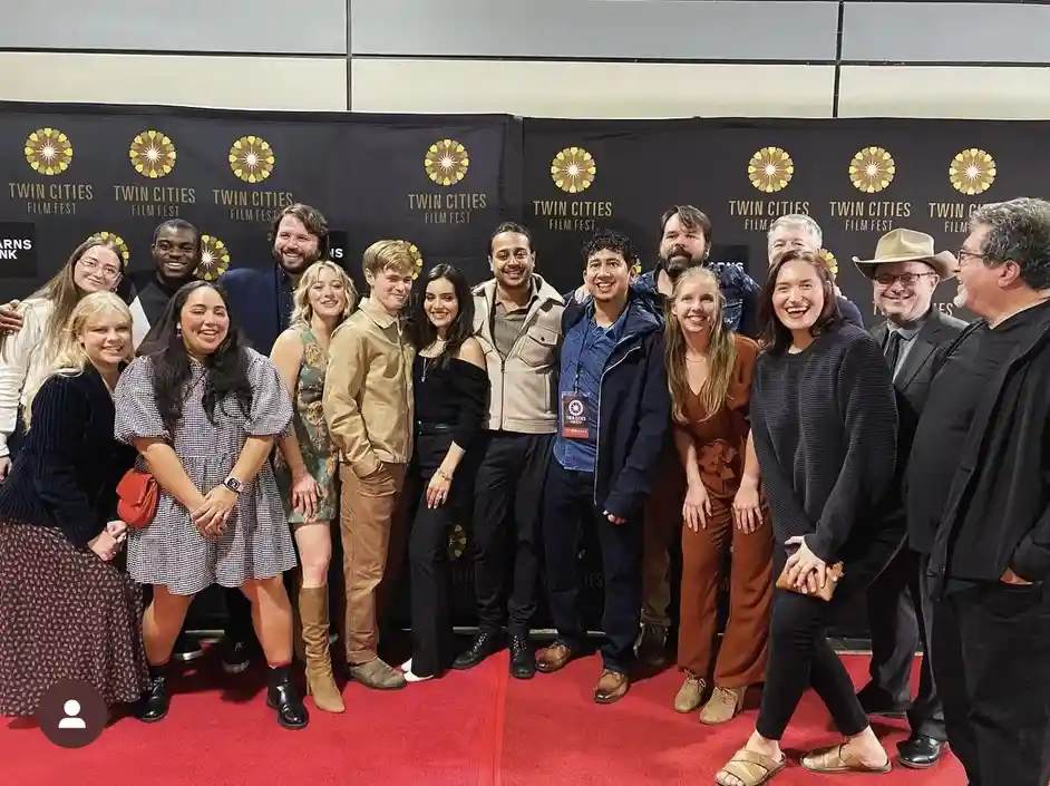 A group of people posing for a photo on a red carpet in front of a black backdrop repeatedly printed with the 'Twin Cities…