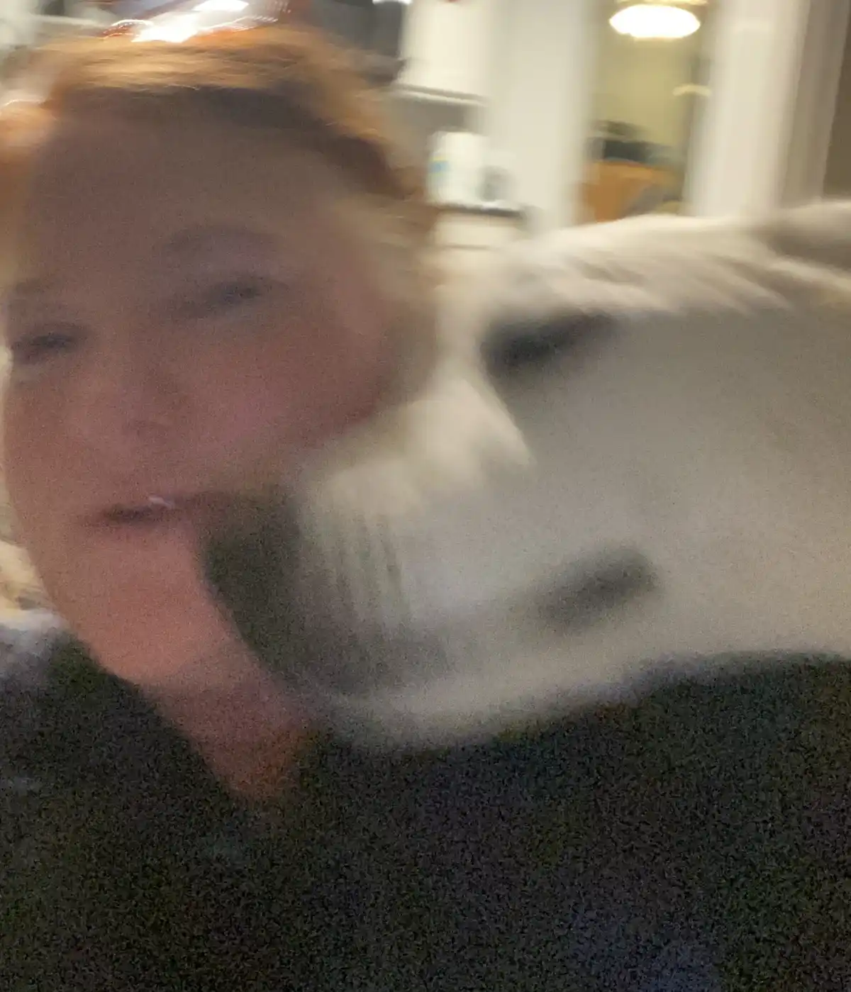 A blurry photo shows a person with reddish hair and a white cat, both appearing to be in motion, likely moving quickly…