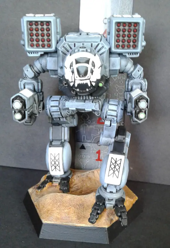 A detailed grey robot figurine with glowing red eyes and a skull-like faceplate stands on a rocky base. The robot has…